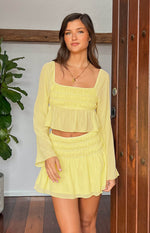 Front view of a yellow chiffon long sleeve top with a square neck, smocked bodice, and sheer flared cuffs