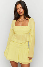 Yellow chiffon long sleeve top with a square neckline, shirred bust, sheer long sleeves, and a peplum hem