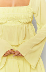 Close-up of the yellow chiffon top's smocked bodice, flowy peplum, and wide bell sleeves
