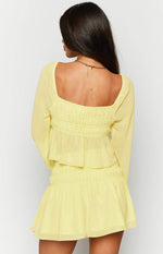 Rear view of a yellow chiffon long sleeve top with a square neckline, shirred back bodice, and ruffled peplum hem