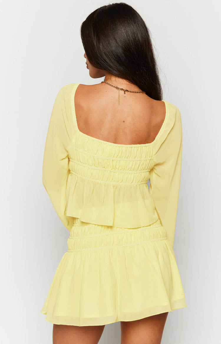 Rear view of a yellow chiffon long sleeve top with a square neckline, shirred back bodice, and ruffled peplum hem