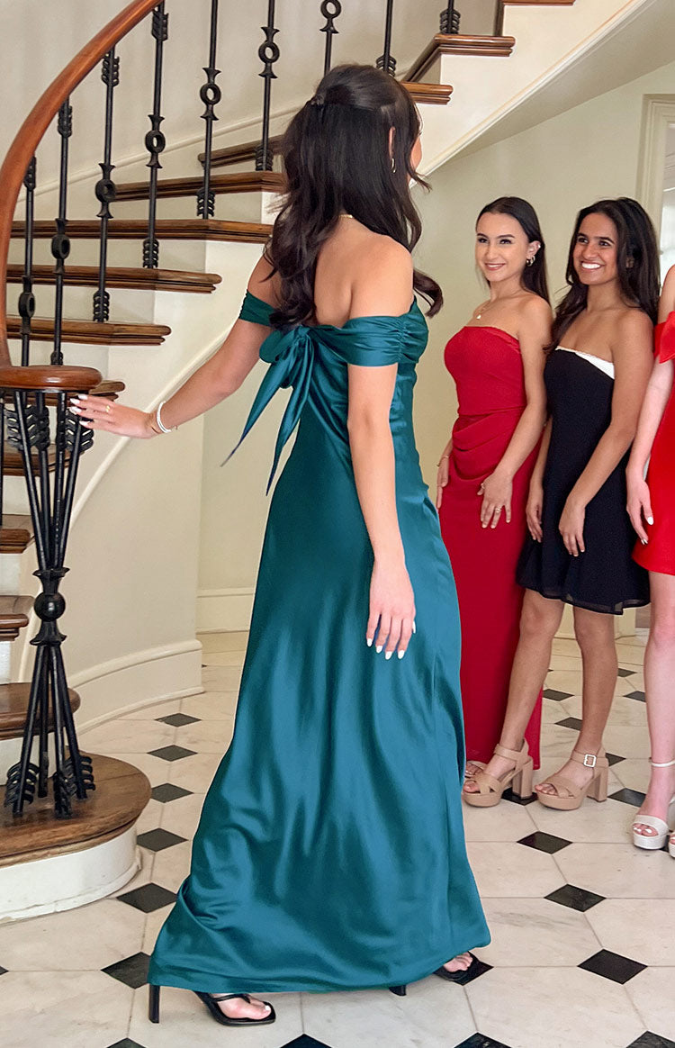 Rear view of a teal off-the-shoulder maxi dress with a large bow tie-back detail and flowing skirt