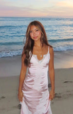 Front view of a pink satin maxi dress with a white lace trim V-neckline and delicate spaghetti straps