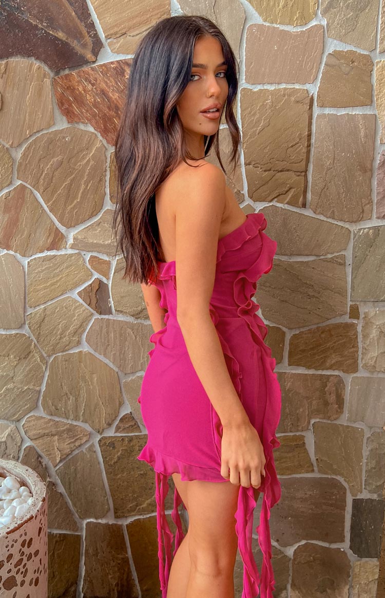 Side view of a fuchsia strapless mini dress with ruffled bodice and long tassel details at the hem