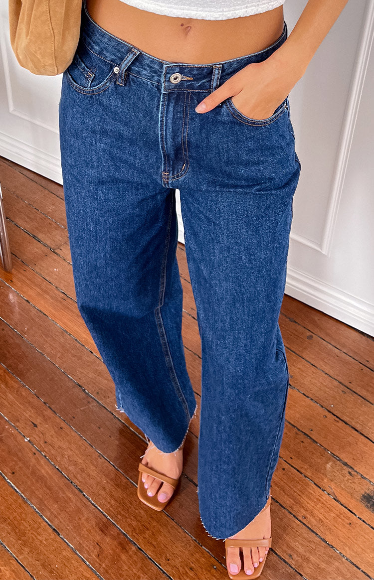 Dark wash wide leg denim jeans with raw frayed hem and front button closure