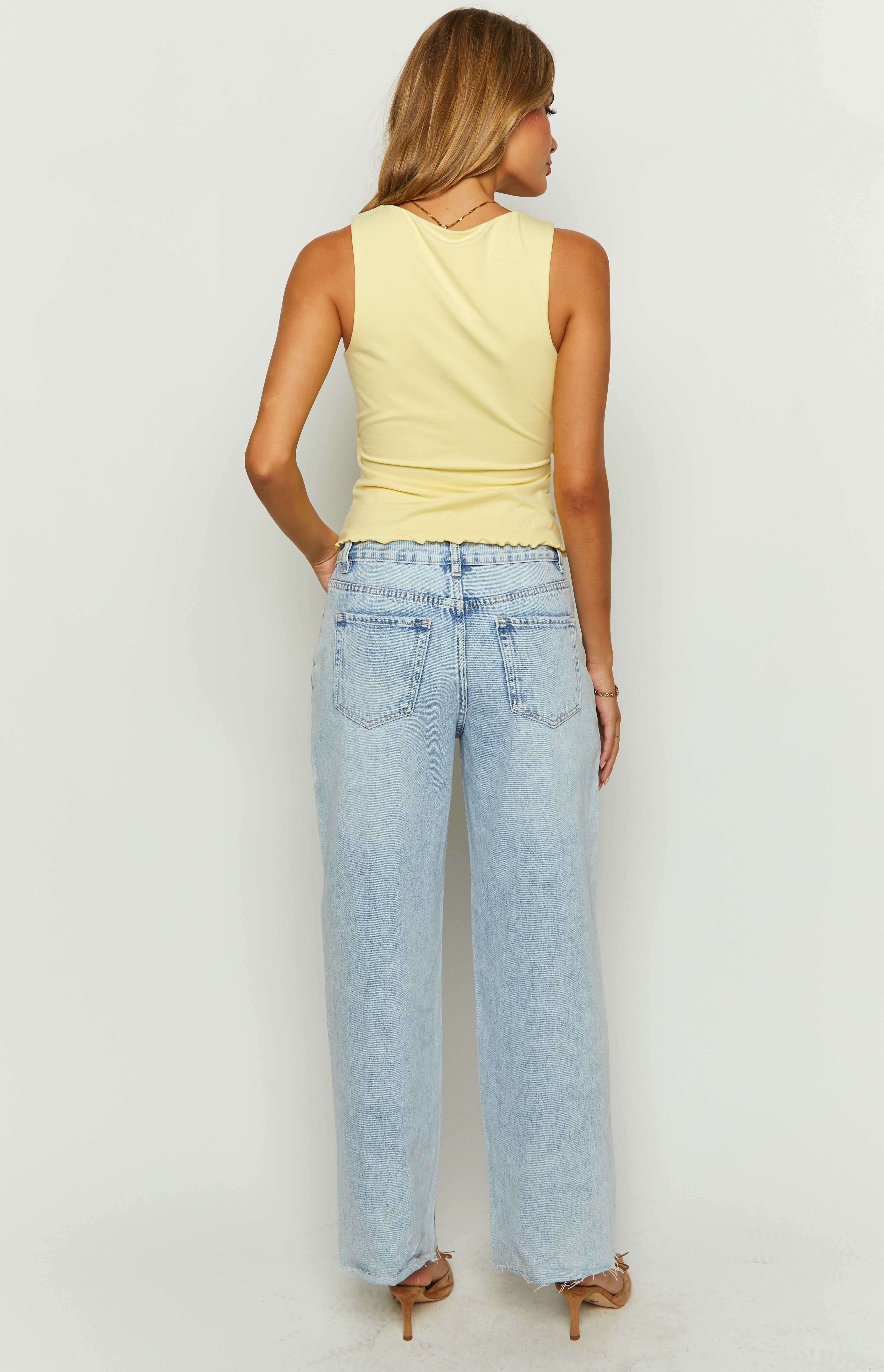 Rear view of light wash denim wide leg boyfriend jeans showing the back pockets and frayed hem
