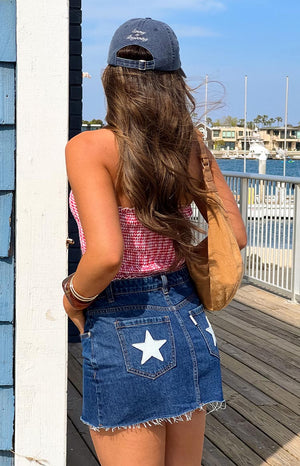 Rear view of a blue denim low rise mini skirt with white star patches on the back pockets and frayed hem