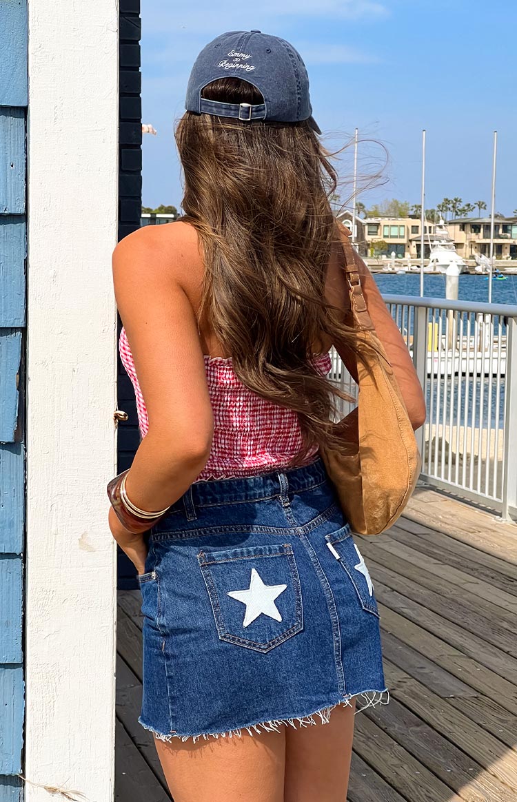 Rear view of a blue denim low rise mini skirt with white star patches on the back pockets and frayed hem