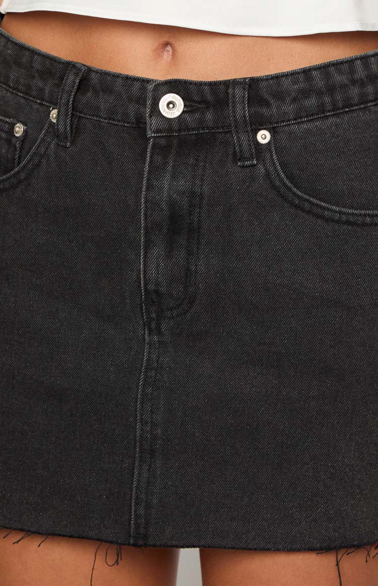 Close-up of the black denim mini skirt's waistband, silver button closure, zipper fly, and front pockets