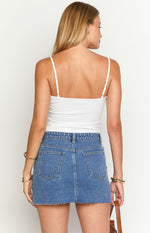 Rear view of a mid wash denim low rise mini skirt with back pockets and a frayed hem