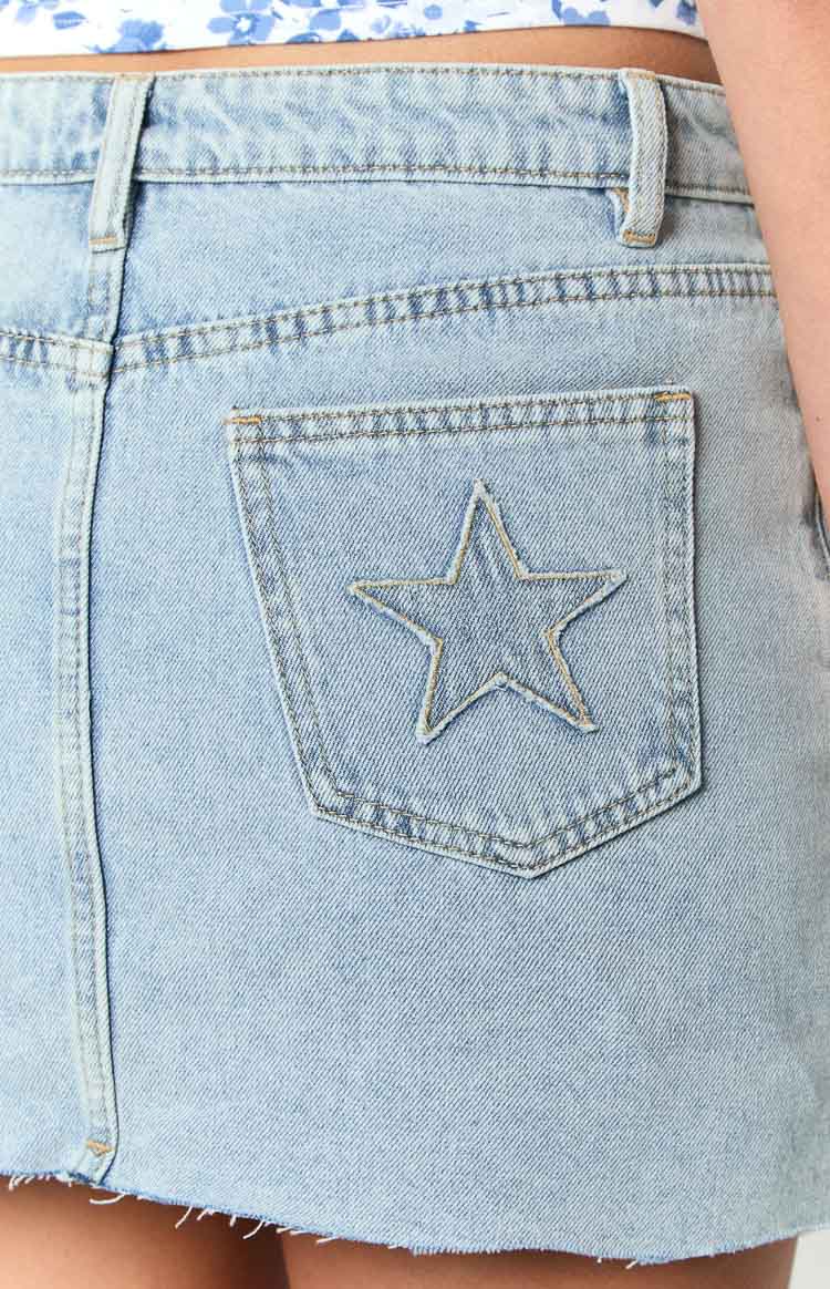 Rear view showing the star embroidered back pocket and raw hem of a light wash denim mini skirt