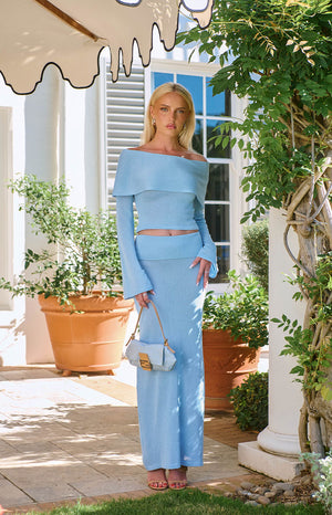 A lifestyle shot of our model wearing a long light blue maxi skirt made from a textured knit material. This maxi skirt features a wide flat waistband.