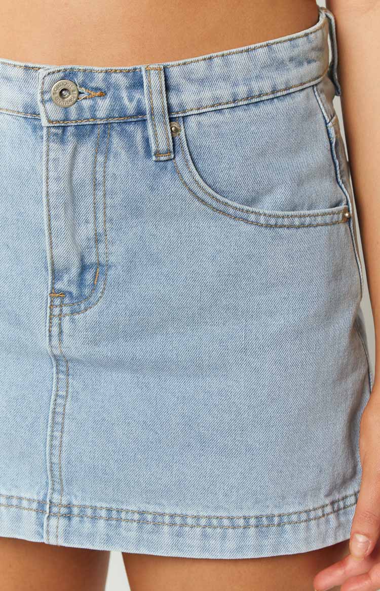 Close-up of the light wash denim skort showing the waistband, button closure, belt loops, and front pocket with contrast stitching