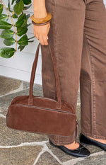 Close-up of a brown suede baguette bag showing the silver top zipper and stitched shoulder straps