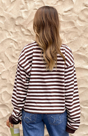 Back view of a person wearing a brown and white striped long-sleeved shirt with a wide loose fit and ribbed cuffs and hem.
