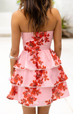 Rear view of a pink floral strapless mini dress with tiered ruffles and white pom-pom trim