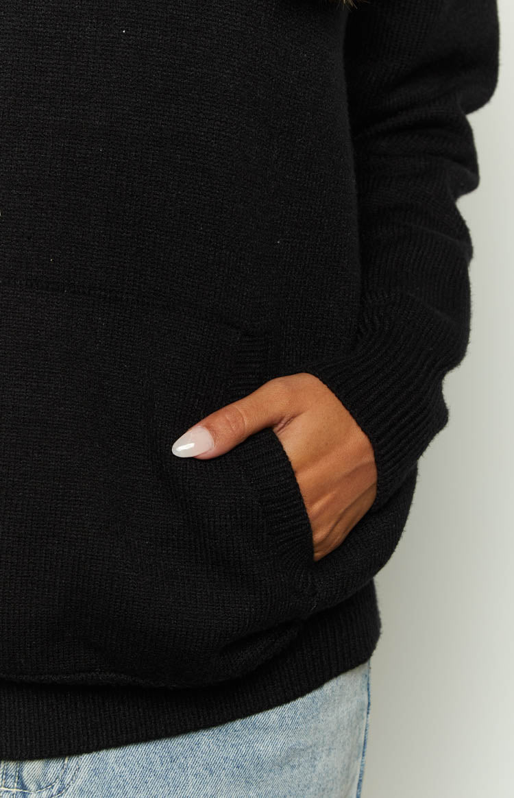 Close-up of the black knitted hoodie showing the ribbed cuff and the kangaroo pocket detail
