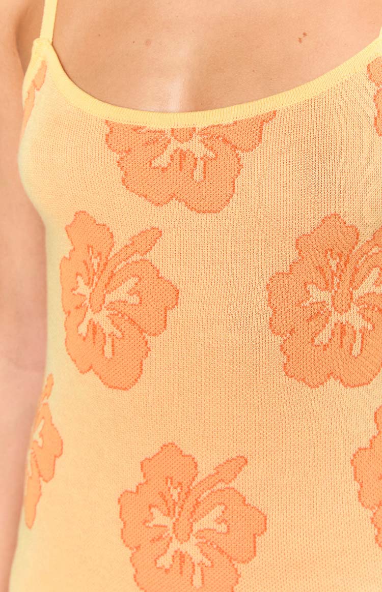 Close-up of the knit texture of the yellow mini dress with an orange hibiscus floral pattern and a thin yellow strap