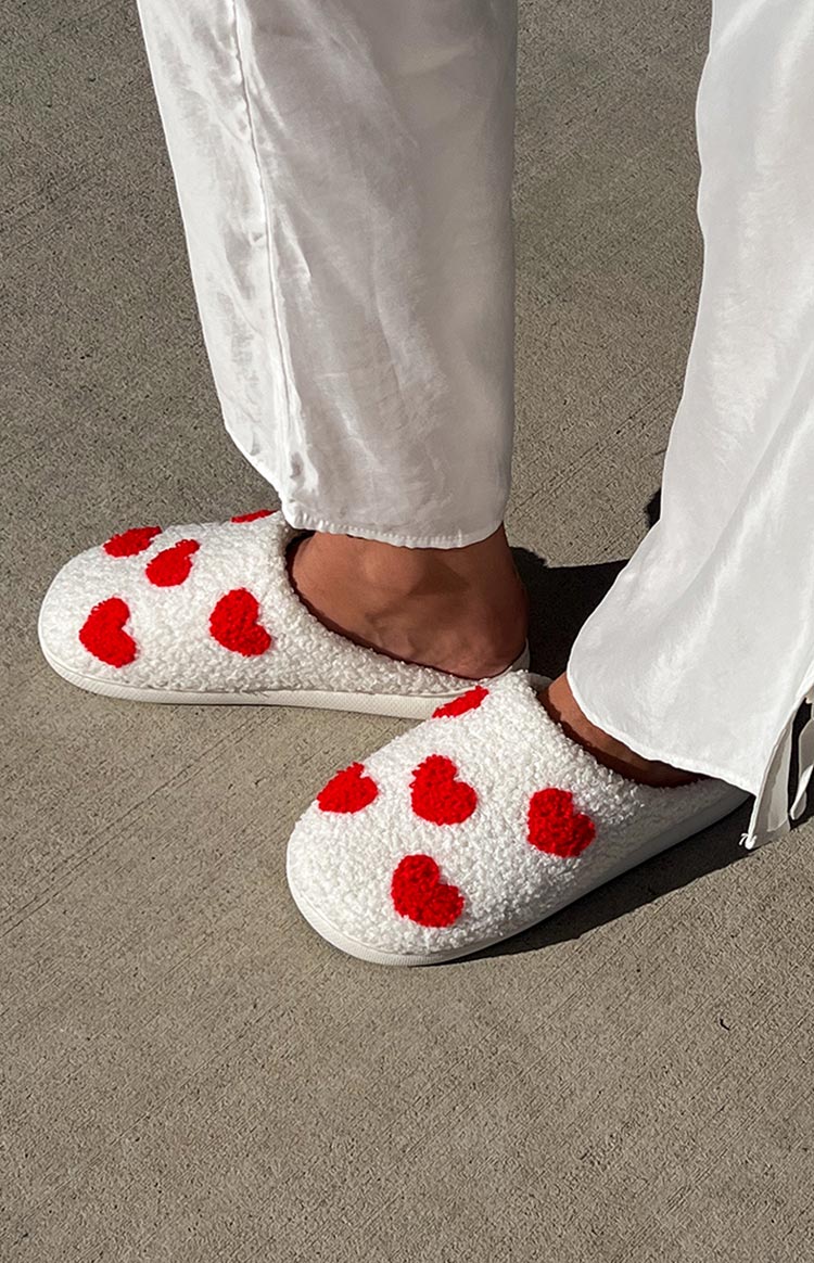 Side view of white fluffy slip-on slippers with red heart patterns