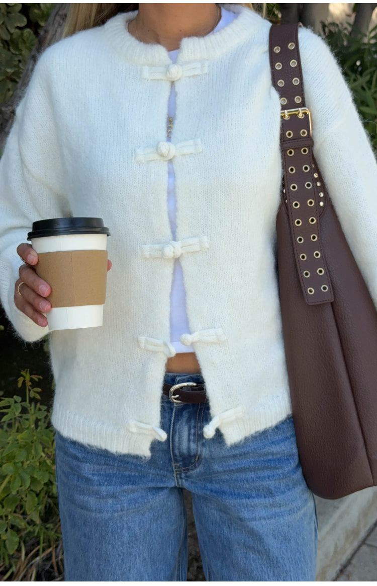 Close-up of the cream knit sweater, showing frog closures and a round neckline