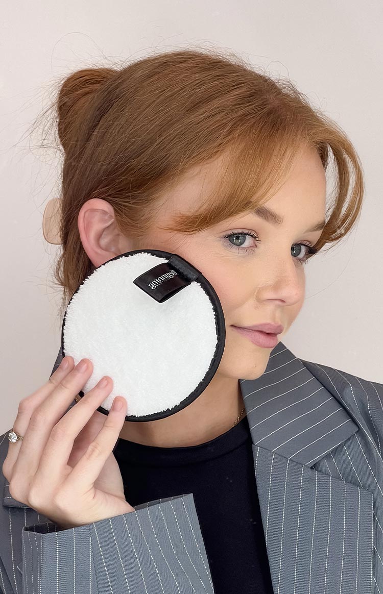 White fluffy reusable face wash pad with black trim and a black loop label