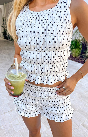 A white shorts with a black polka dot pattern, featuring tiered ruffles and an elasticated waistband. Perfectly with sleeveless crop top with tiered ruffles in a white and black polka dot print, designed to be part of a matching set.