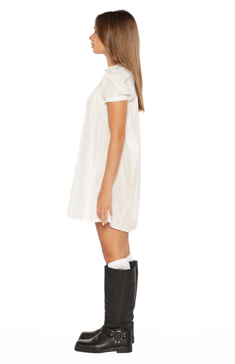 Side view of a white sheer mini dress with a relaxed fit, short puff sleeves, and lace trim on the neckline and sleeves