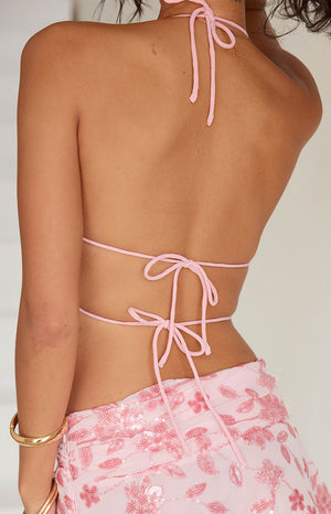 A rear view of our model wearing a pastel pink halter top with a tie closure at the neck and a second tie at the mid-back.