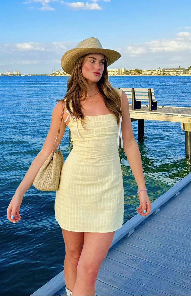 Front view of a fitted yellow mini dress with a square neckline, thin shoulder tie straps, and subtle vertical stripe texture