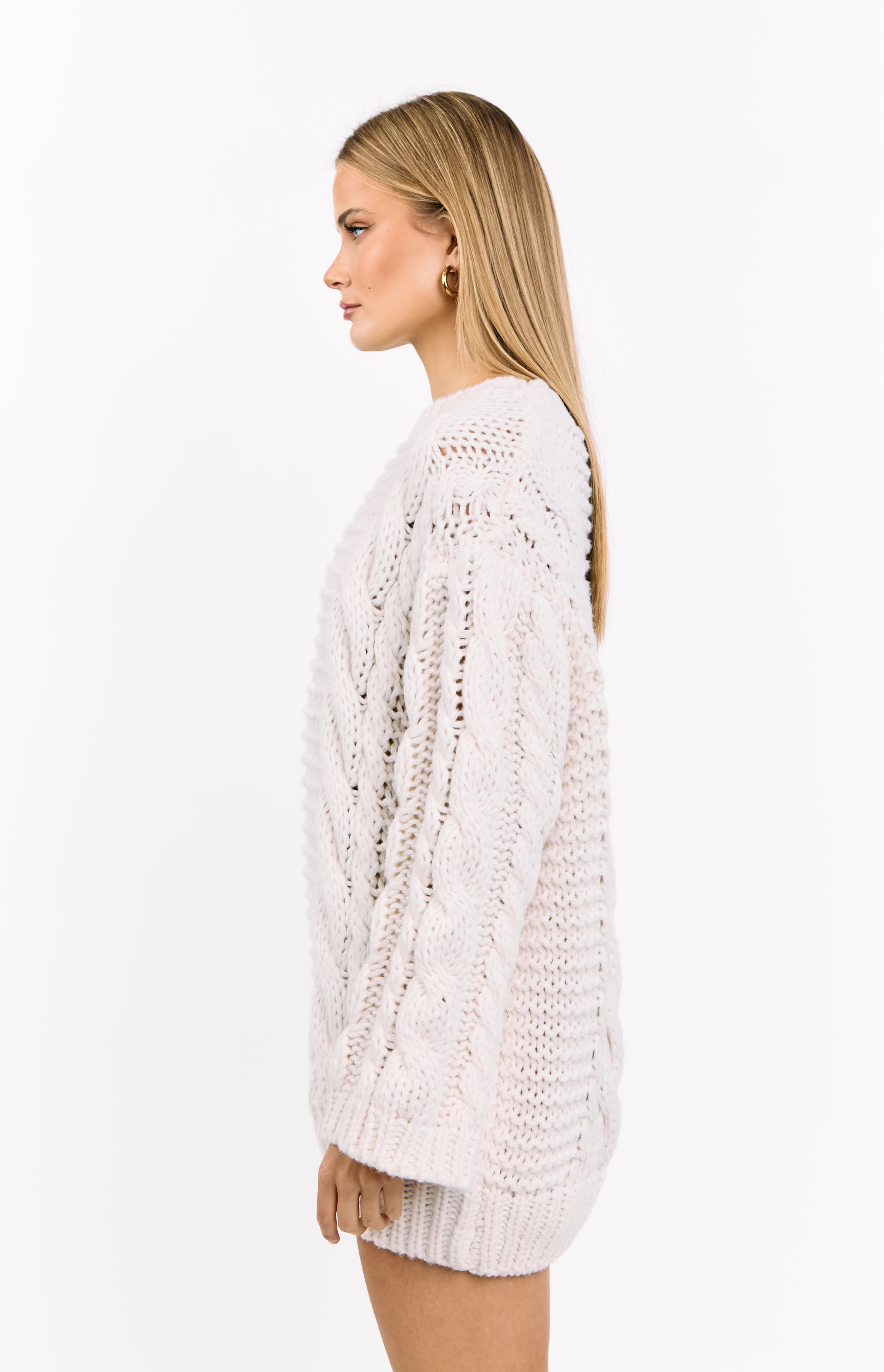 Side view of an oversized cream cable knit sweater dress with chunky texture