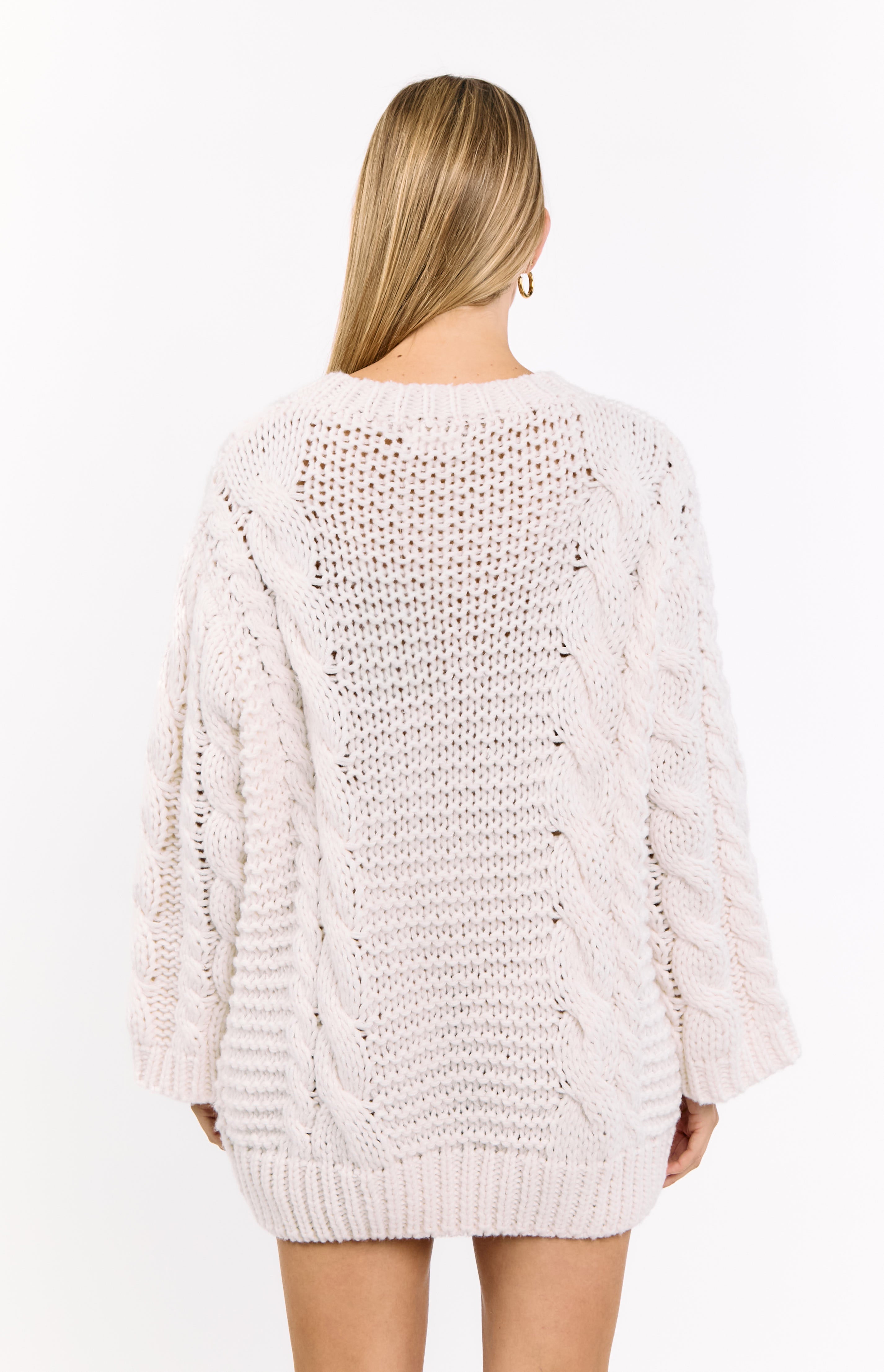Rear view of a cream cable knit sweater dress with an open knit pattern and round neckline