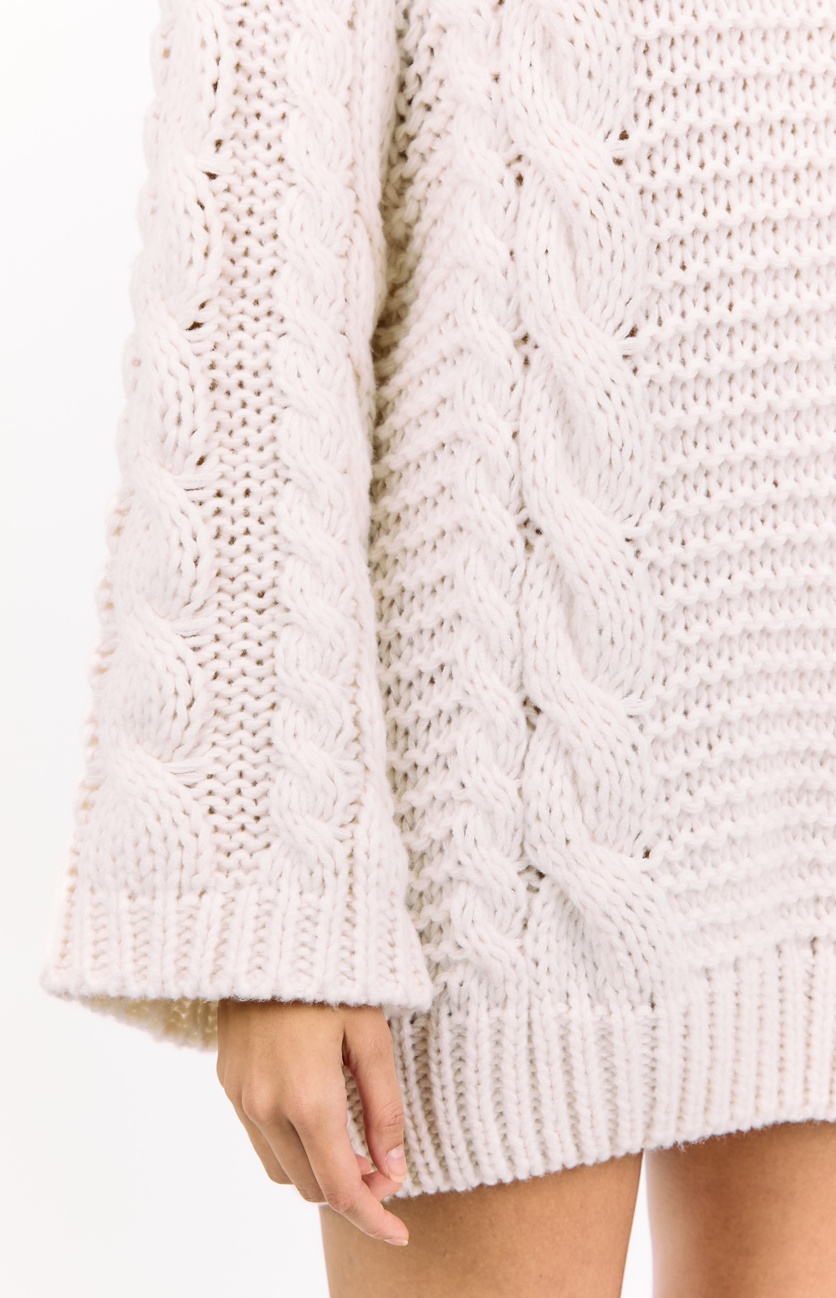 Close-up of the cream cable knit pattern on the sleeve and body of the sweater dress with ribbed cuffs and hem