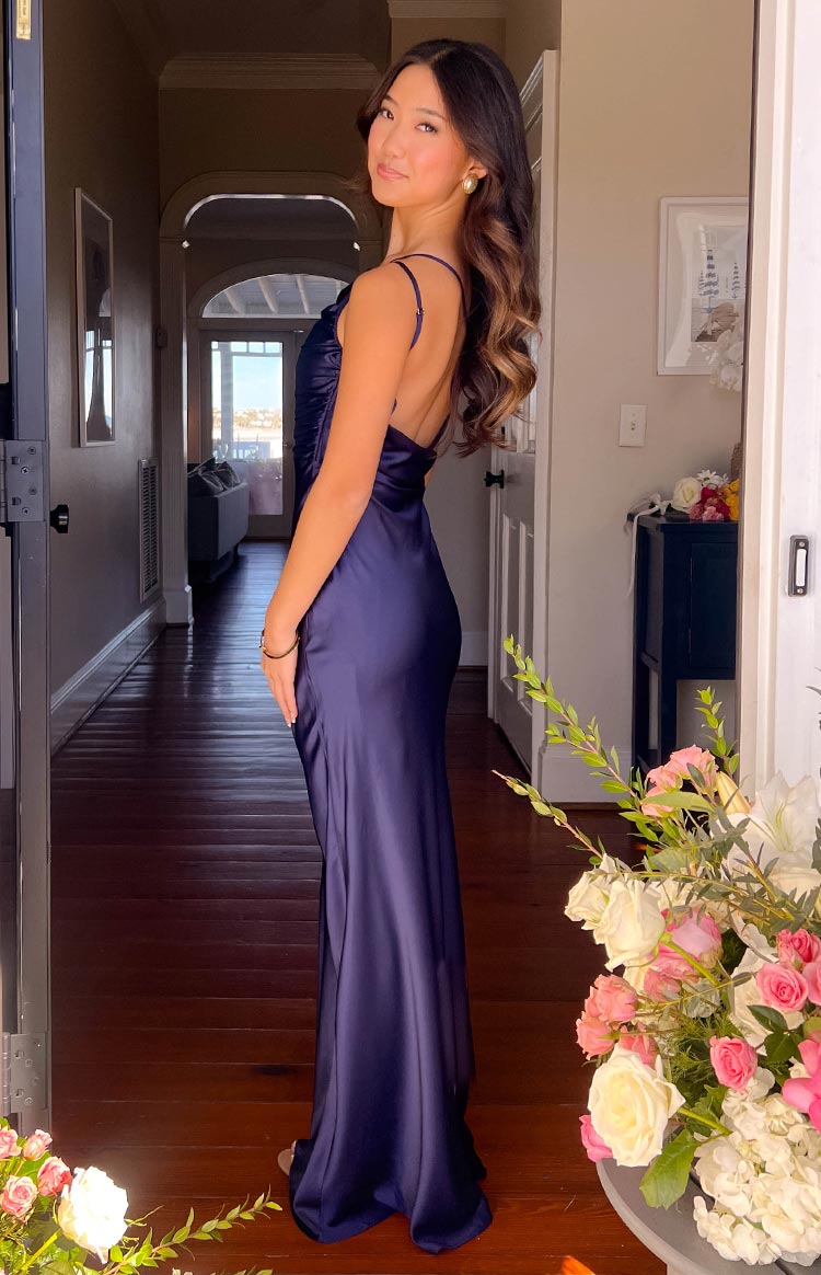Side view of a navy satin maxi dress with a fitted silhouette and a low scoop back with thin spaghetti straps