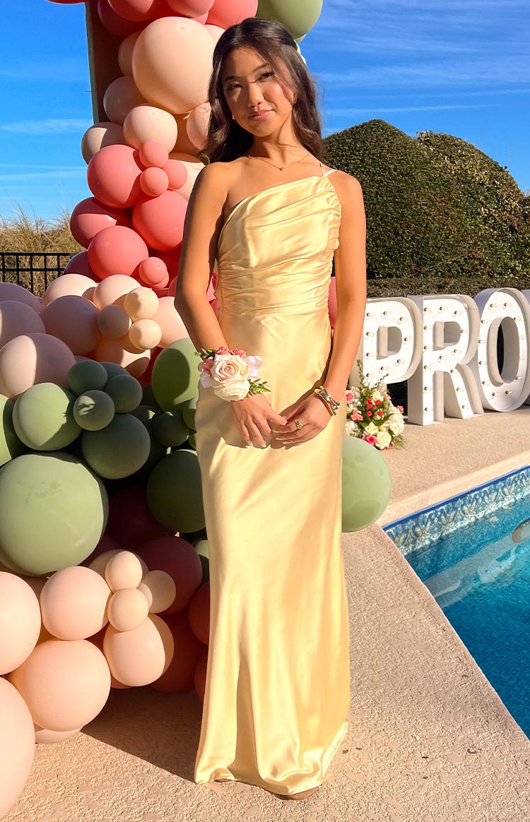 Full-length front view of a light yellow satin one-shoulder maxi dress with a draped bodice and flowing skirt