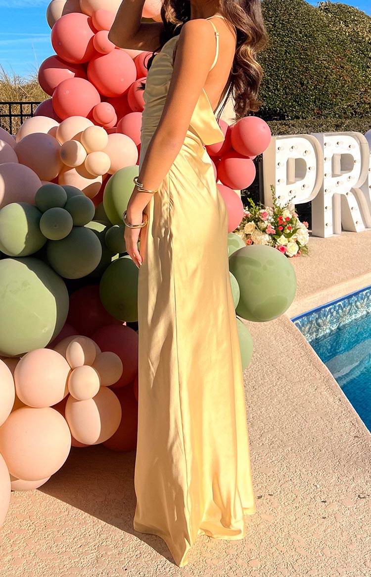 Side view of a yellow satin maxi dress showing the low back, thin spaghetti straps, and ruched side detail