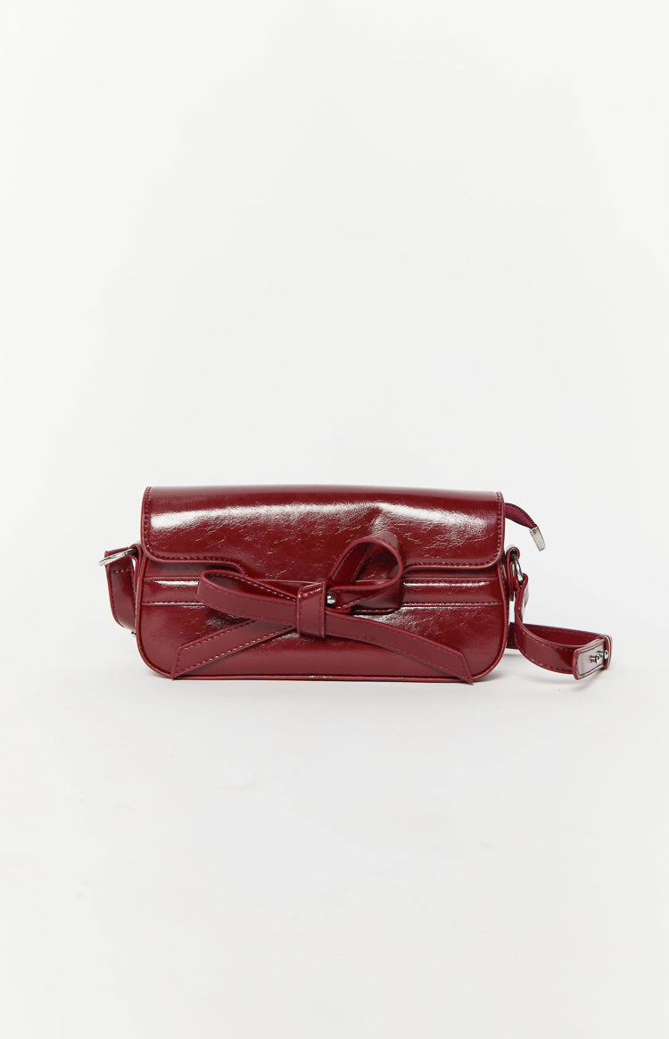 Front view of a red patent PU shoulder bag with a decorative bow on the flap closure and an adjustable strap