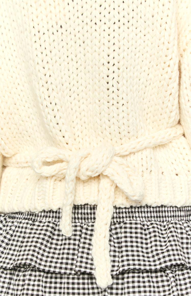 Close-up of the cream chunky knit cardigan with a braided tie-waist detail tied into a bow