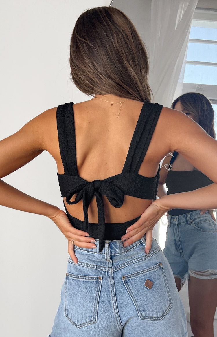 Rear view of a black textured top with wide shoulder straps and a tie-back bow detail
