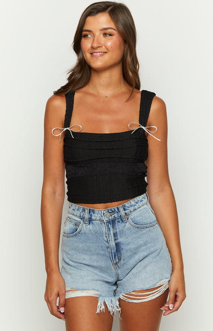 Front view of a black textured crop top with a square neckline and white bow details on the wide straps