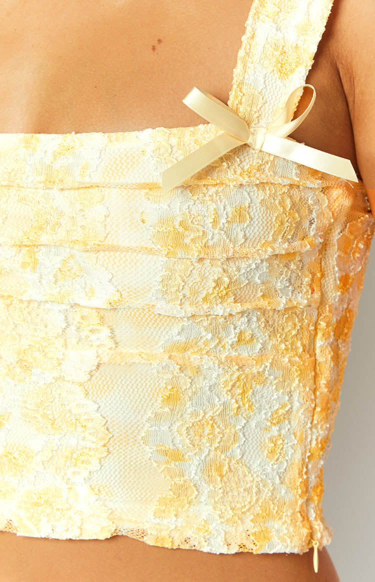 Close-up of the yellow floral lace top showing horizontal gathered details and a small yellow satin bow on the strap