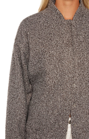 A close-up of a collarless jacket made of a thick textured brown and grey bouclé fabric with a hidden button placket.