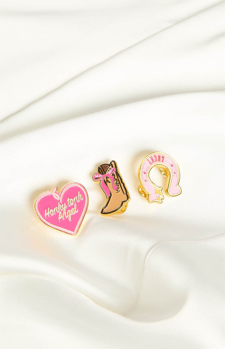 Three enamel pins including a pink heart with 'Honky tonk Angel', a brown cowboy boot, and a pink horseshoe with 'LUCKY'