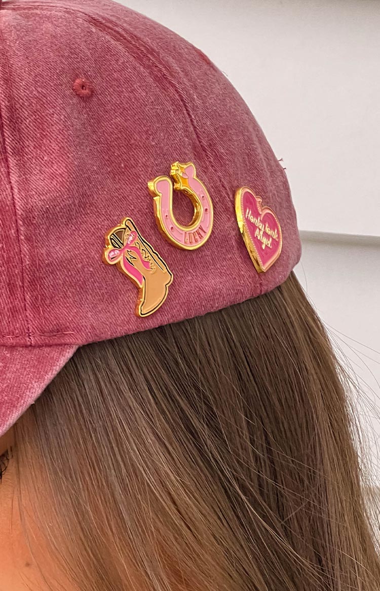 Close-up of three gold and pink enamel pins: a cowboy boot, a horseshoe with 'LUCKY', and a heart with 'Honky Tonk Angel'