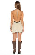 Rear view of the white mini dress with a deep scoop back, bronze sequin trim, and halter neck tie closure