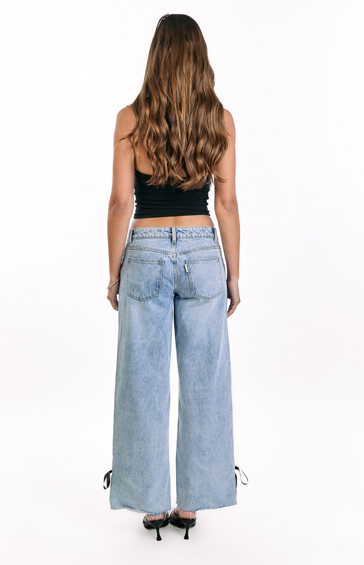 Rear view of light wash denim low rise wide leg jeans with back pockets and black bow ties at the frayed hem