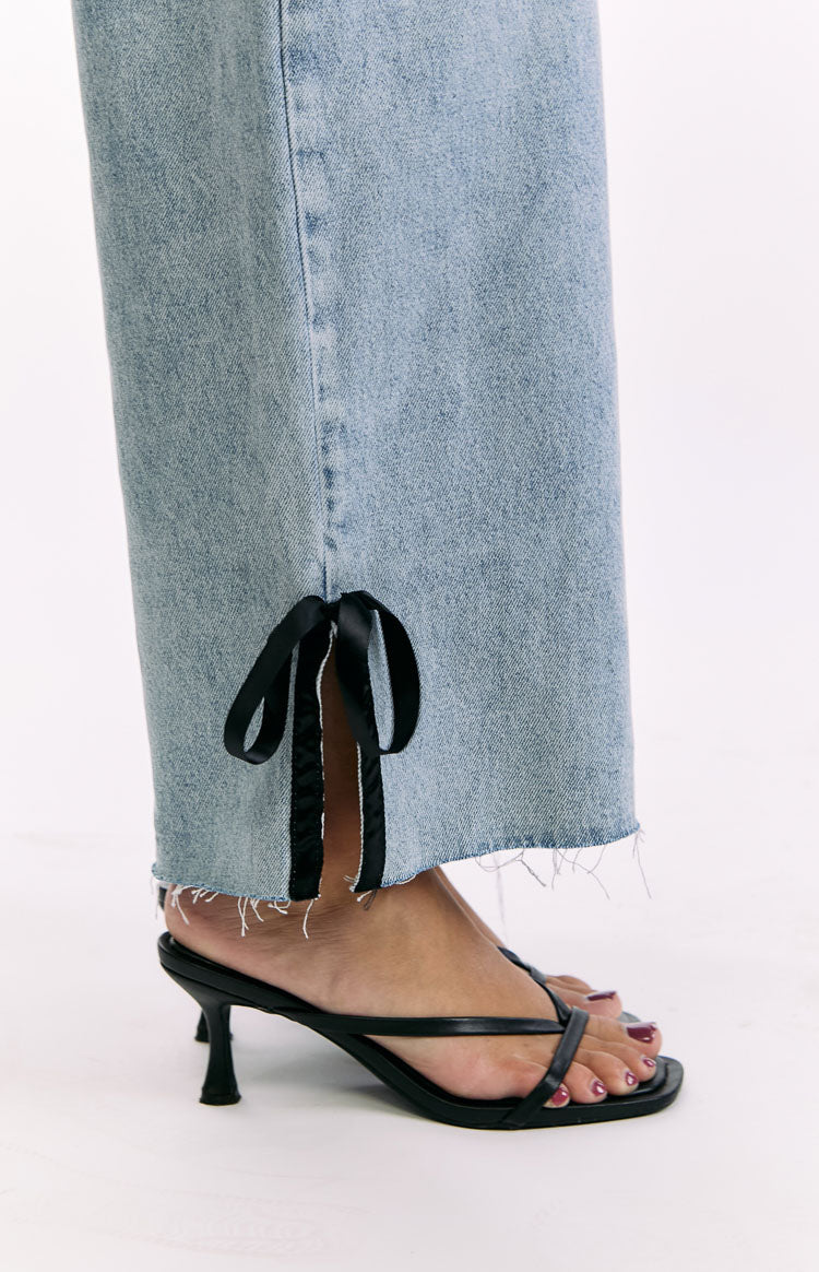 Close-up of the raw-cut hem of light wash denim jeans with a side slit tied by a black satin bow