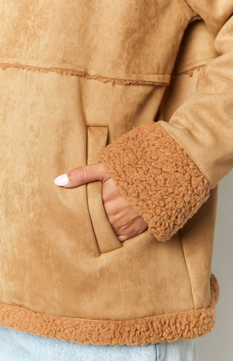 Detail shot of the brown suede jacket's side pocket, showing the fluffy faux fur trim on the cuff and hem