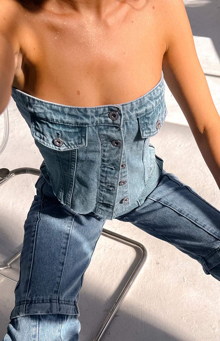 Close-up of the mid wash denim strapless top with button-front closure, chest flap pockets, and raw frayed hem