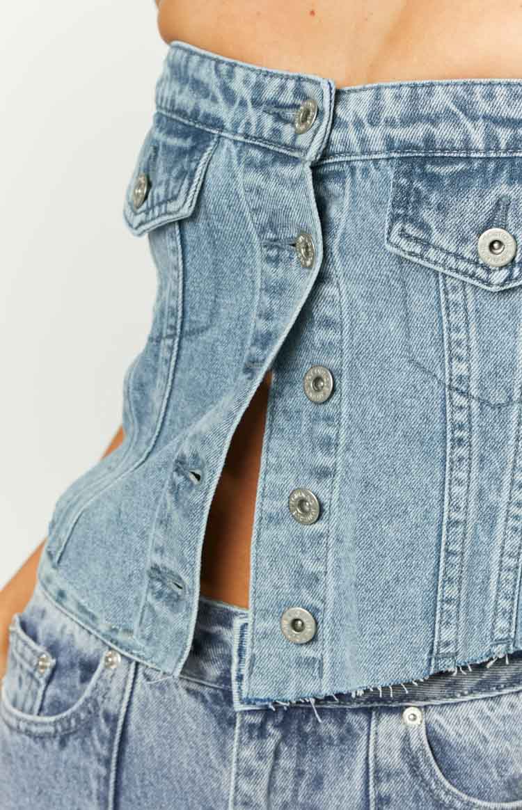 Close-up of the side of a mid-wash denim button top, showing unfastened silver buttons and a raw frayed hem
