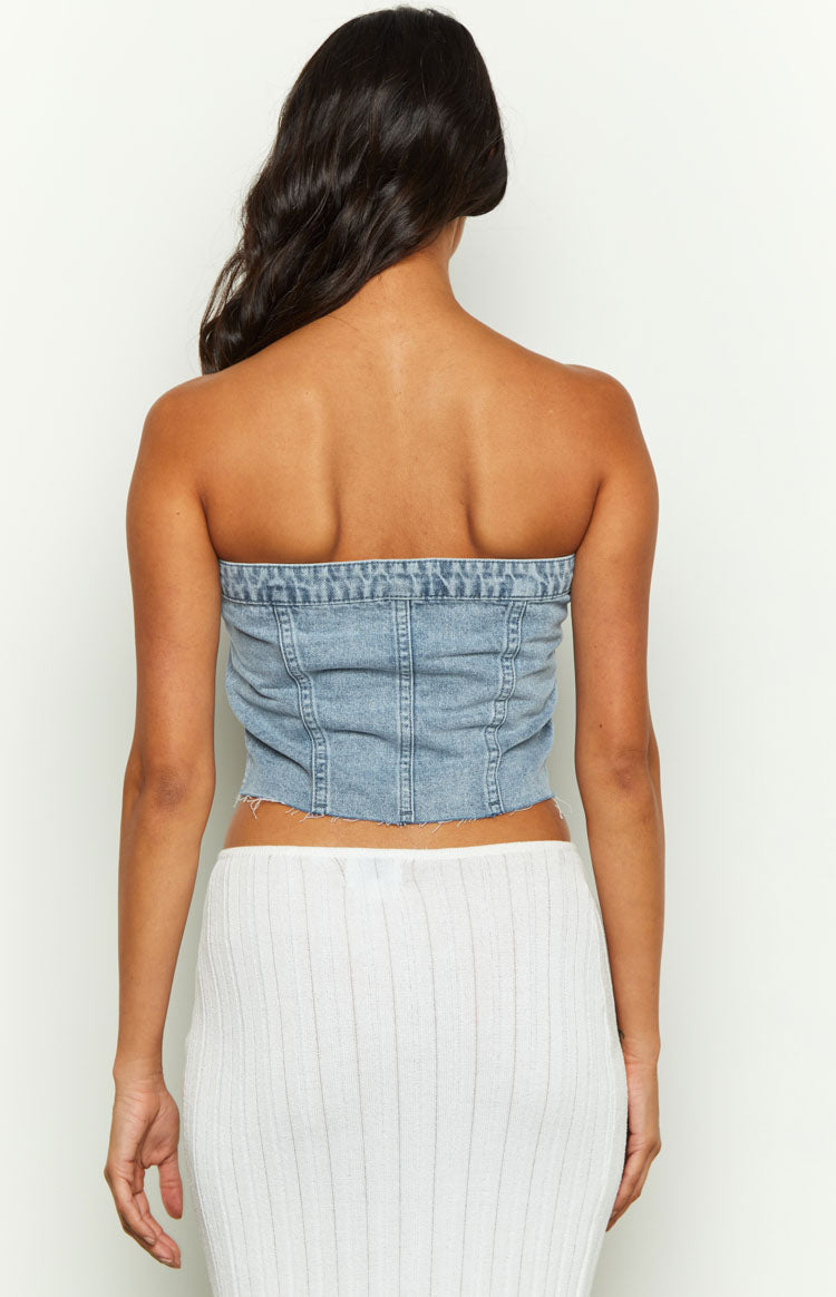 Rear view of a light blue denim strapless top with vertical seam detailing and a raw hem